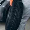 Homem com pneu do carro na mão.