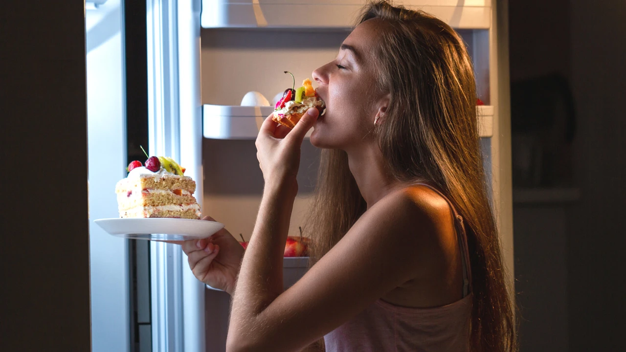 Mulher comendo à noite na geladeira.