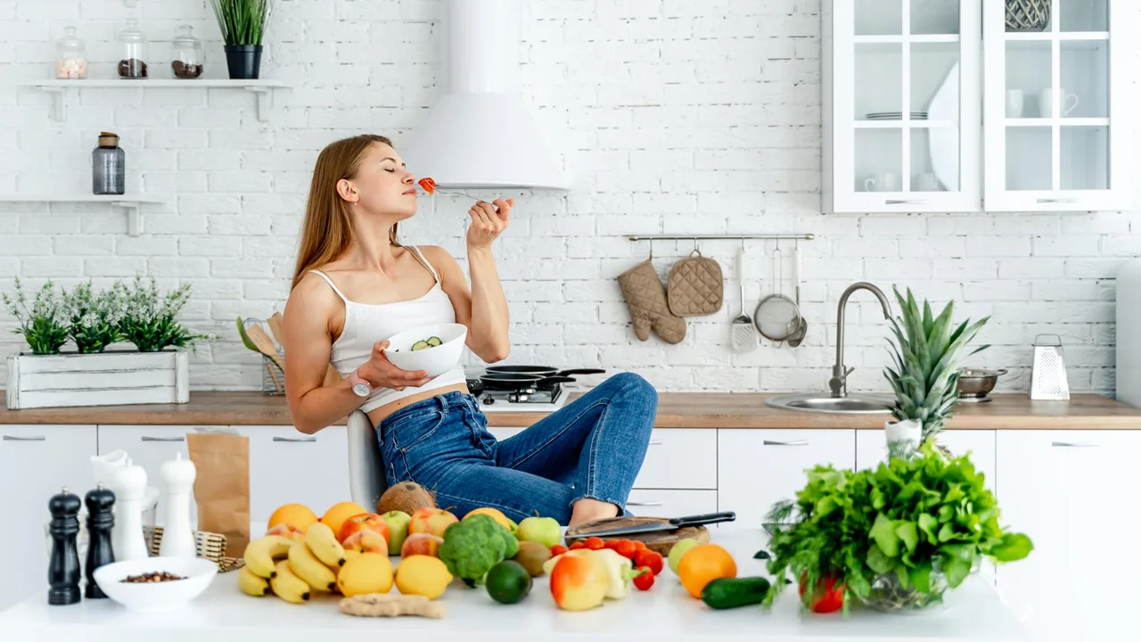 Mulher comendo na cozinha alimentos saudáveis.