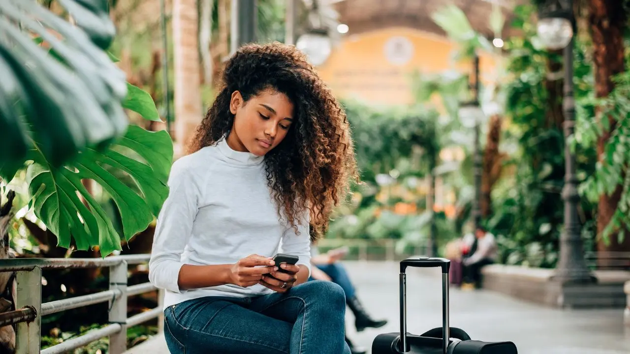Mulher com mala de viagem e celular.